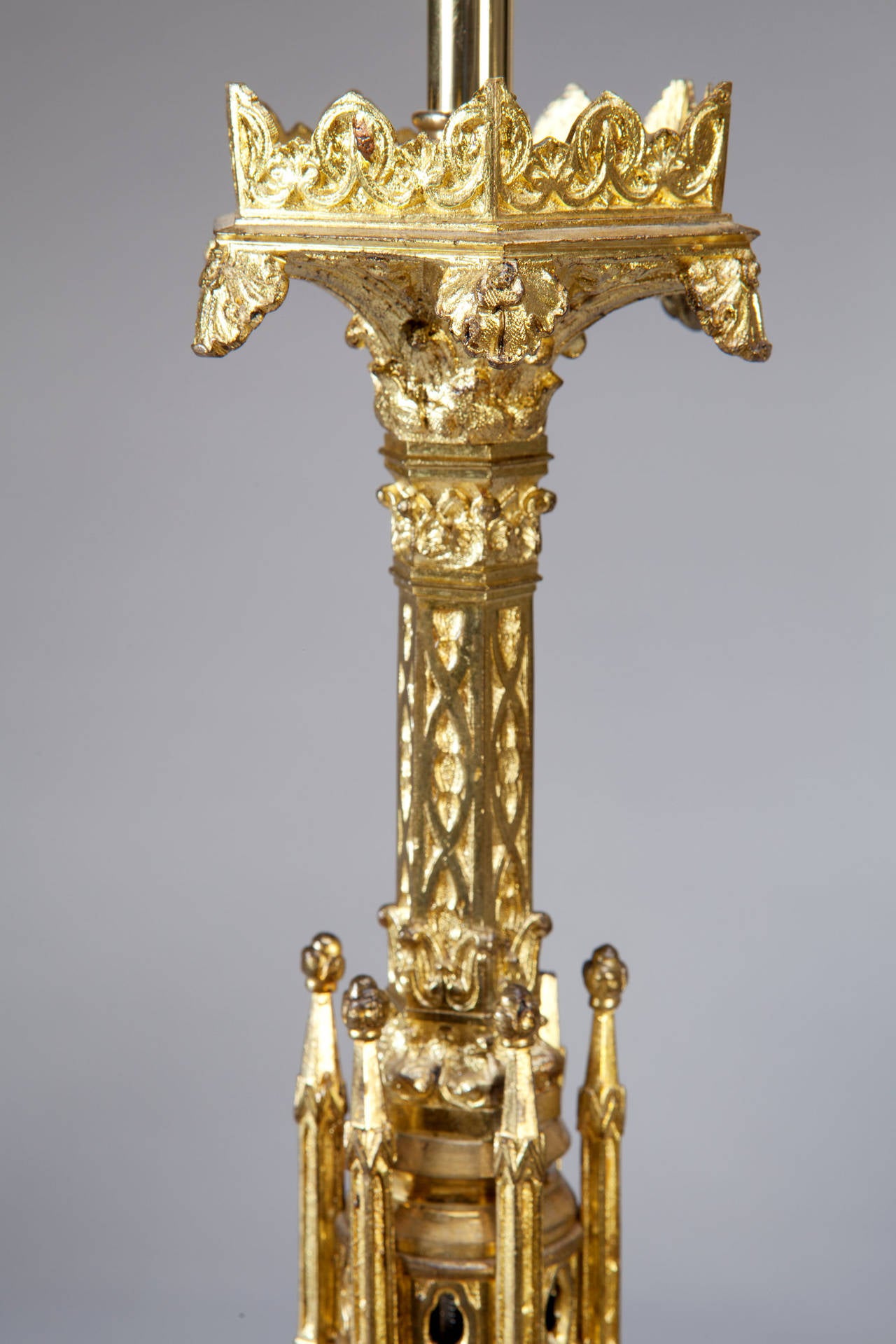 Pair of Louis Philippe lacquered brass Gothic pricket candlesticks now converted to lamps. Each fashioned as a spire with flying buttresses, Gothic traceries and pierced elements. The triangular bases have canted corners and each face is decorated