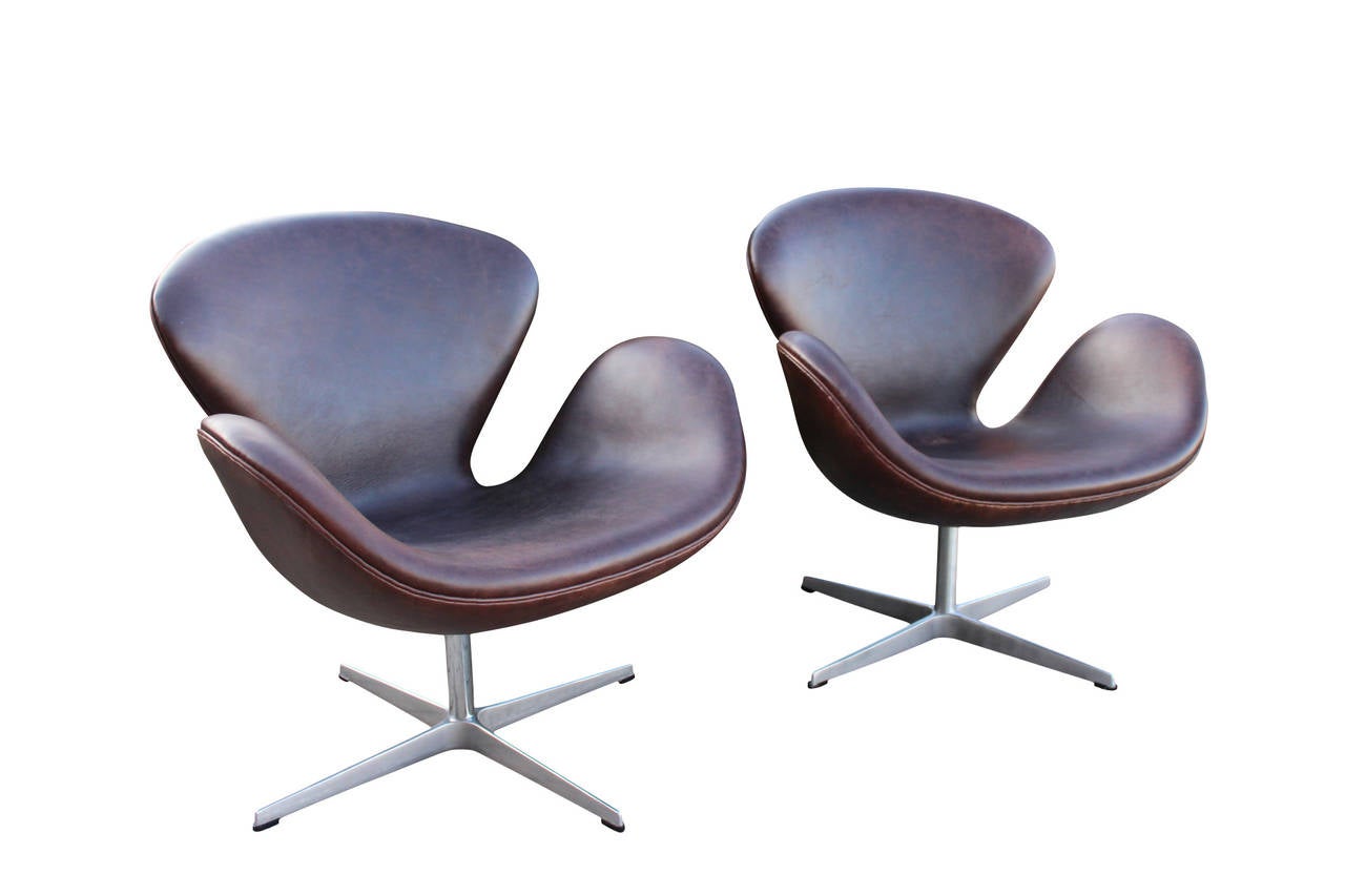 A pair of Swan chairs, model FH 3320, in dark brown patinated leather. The chairs were designed by Arne Jacobsen in 1958 and manufactured by Fritz Hansen in 1999.