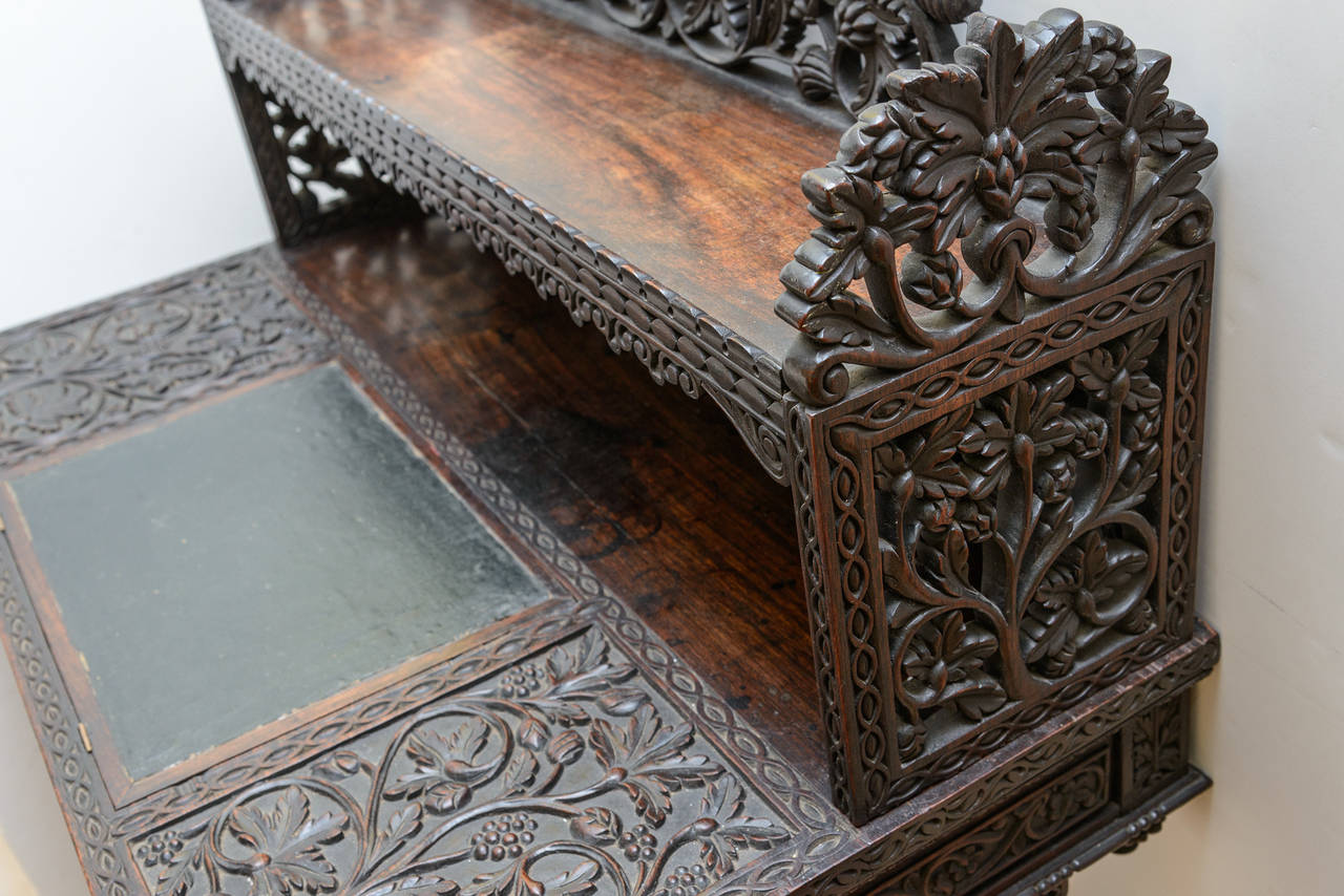 19th century hand-carved desk profusely carved with snakes within the side panels. The piece is raised upon full figures of tigers. The desk features an inset leather top which lifts for an interior compartment. The desk is fitted with two bottom