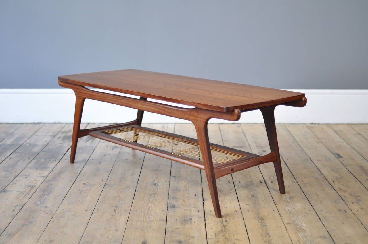 Long teak coffee table with an individual aesthetic provided by the sculptural frame and the original rattan shelf. The tabletop flips over to reveal a veneered surface with heat protection.