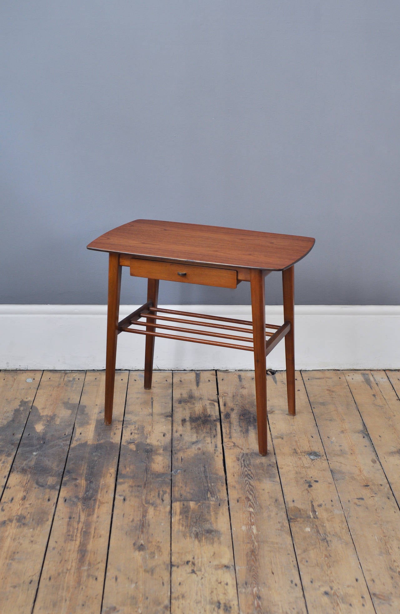 Danish side table with perfect sizing to be a night stand or telephone table. It has an elegant simplicity to its design with delicate features including the spindle magazine rack and brass pull.