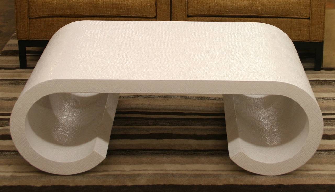 Iconic Mid-Century Modern coffee table features a wrapped scroll form with a lightly textured surface, newly finished with glossy white lacquer. The softly curving upper waterfall edges end in a C-slab leg with an inward roll. The crisp white