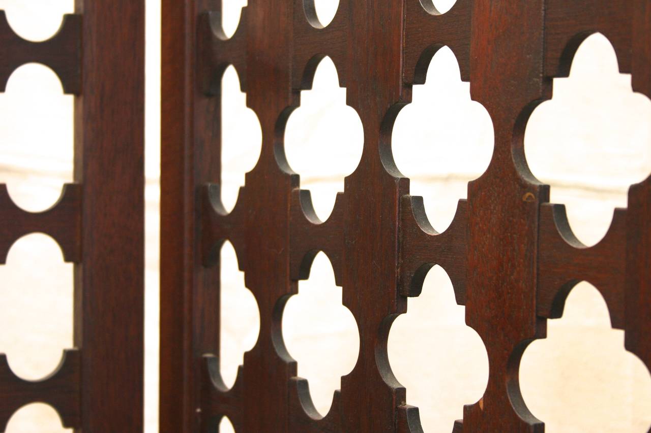 Four-panel modern room divider screen. Intricately carved geometric design creates a pattern of 4-inch medallions in dark wood and negative space. Arch and spire shaped details on lower edges evokes Moorish aesthetic. Solid teak with brass hinges.