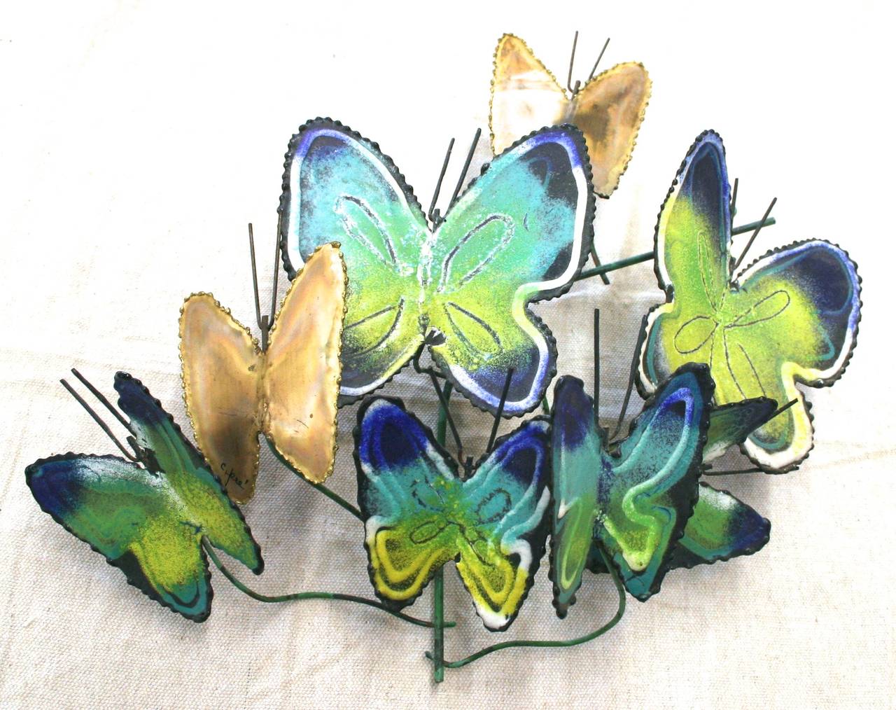 Wall-mounted butterfly sculpture signed by Curtis Jere, made of brass and enamel. Shiny brass butterflies mingle with blue, green and yellow enameled hues. This playful piece adds a touch of motion to your wall. Mounts to wall with green wire frame.