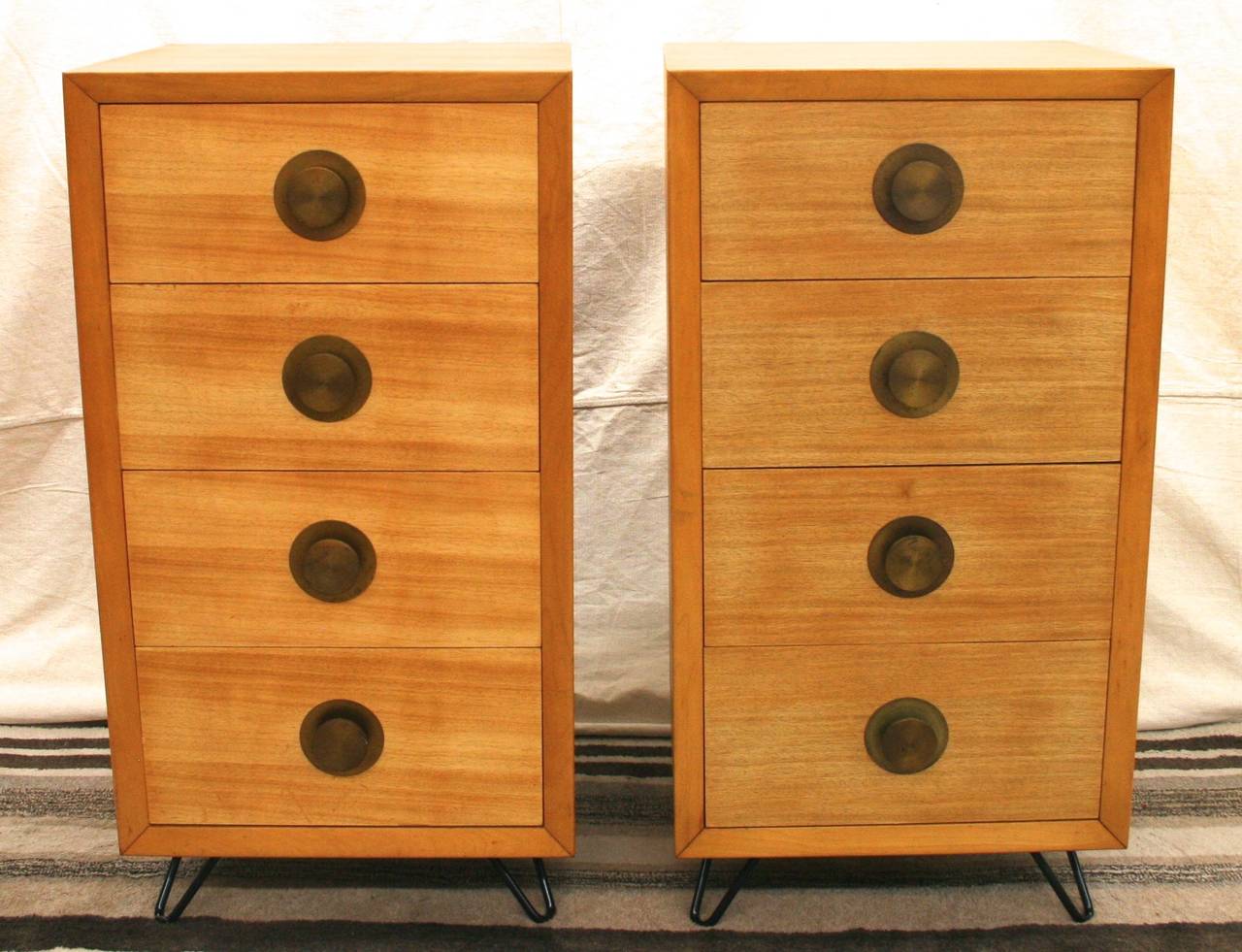 Tall chests or nightstands with four drawers and large brass saucer pulls. Top drawers have a small divided subsection. Stand on a low profile metal hairpin legs.