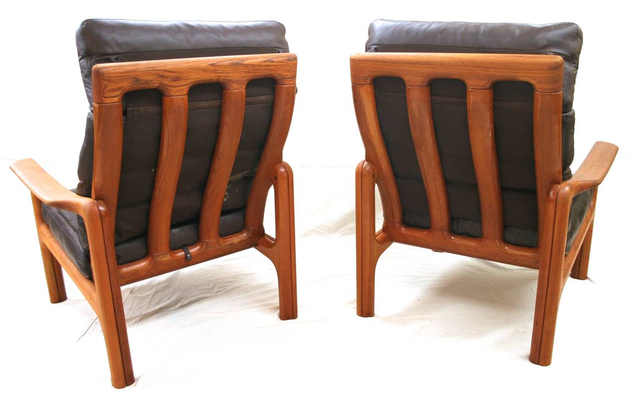 Scandinavian Mid-Century Modern style high back lounge chairs with open frame, crafted from solid teak. Gracefully sculpted frame with comfortable contours. Brown leather cushions with articulated back and headrest.