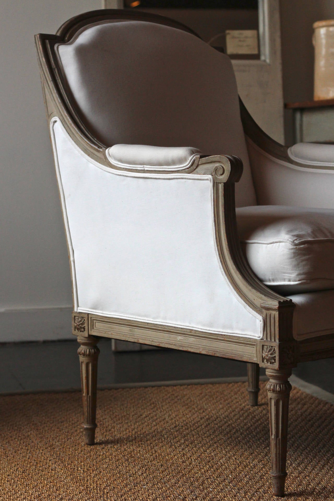 Pair of bergeres with pretty carvings on frame. Painting in soft taupe color.  Seat height is 19 inches.