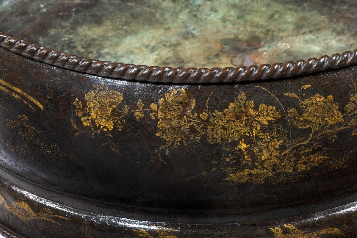 The rope-twist edge above an oval body decorated with cranes and figures within landscapes on a simulated tortoiseshell ground, flanked by carrying handles. 

The taste for lacquer and lacquered wares emerged in England during the reign of Charles