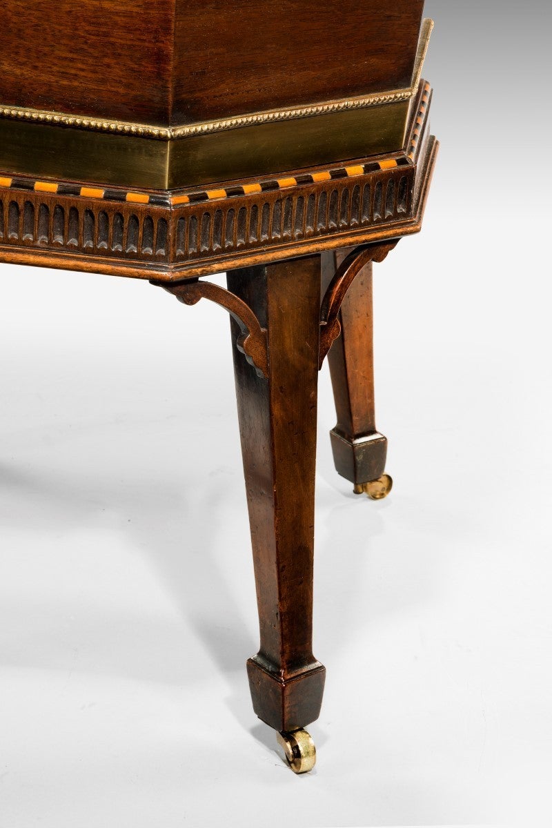 A George III octagonal mahogany wine cooler or cellarette, crossbanded in rosewood, boxwood and ebony. Retaining the original horizontal brass bandings, with unusual pearl beaded borders. Flanked by a pair of carrying handles. Raised on a stand with