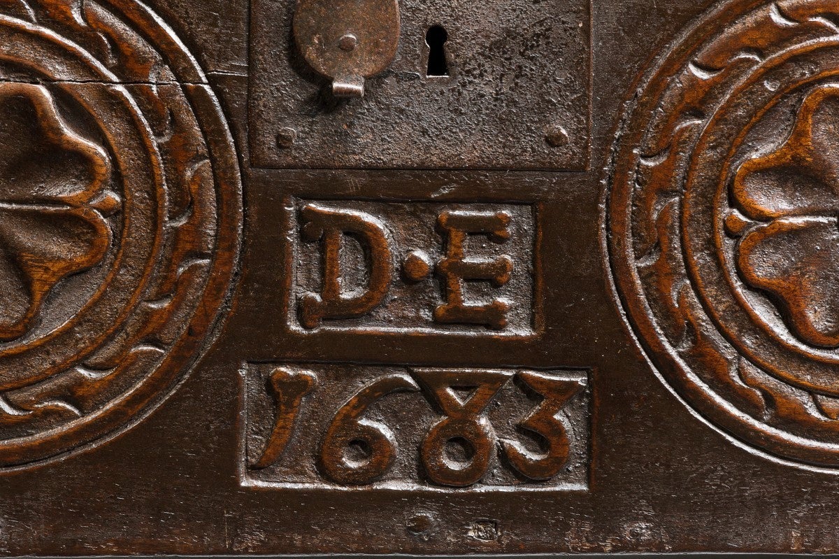 With the initials ‘D.E’ and the date ‘1683’ carved on the front. Decorated with two carved flowers surrounded by carved circular decoration. With a hinged lid.