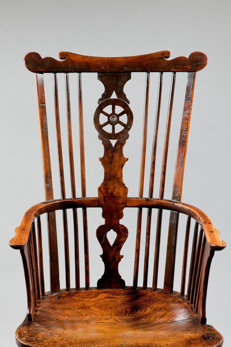 A high-back double bow elbow chair made from yew wood. The central splat has a fretted wheel design. With crook arms and shaped seat. 

Windsor Chairs: The term Windsor Chair is used to describe wooden chairs whose axis of construction is the seat