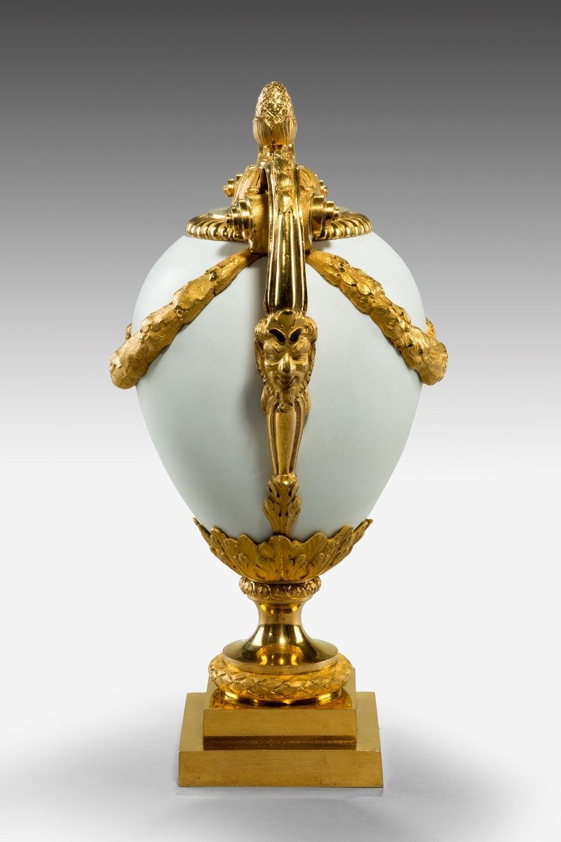 By Matthew Boulton (Boulton & Fothergill, Soho Manufactory, Birmingham) 
White opaque glass by James Keir 

An ornamental vase, with a pine cone finial, leaf motif, gadrooned rim, oak-leaf swags and pendants on the body. With satyr’s masks on the