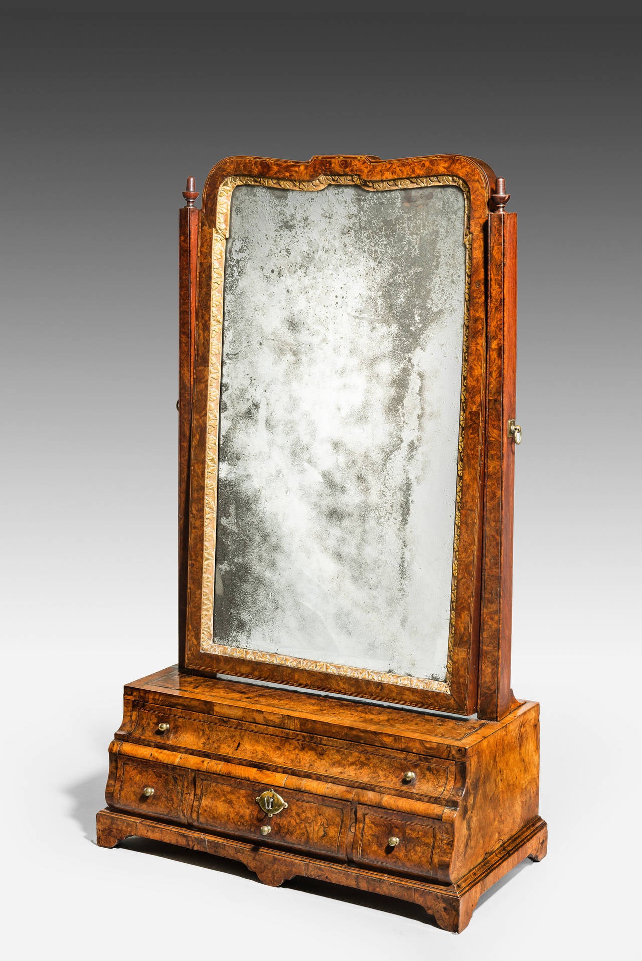 Provenance: Slebech Hall, Pembrokeshire.

In burr walnut. With the original bevelled rectangular glass set in a shaped and moulded mirror frame with a gilded carved inner slip. The square upright supports topped with replaced carved finials, and