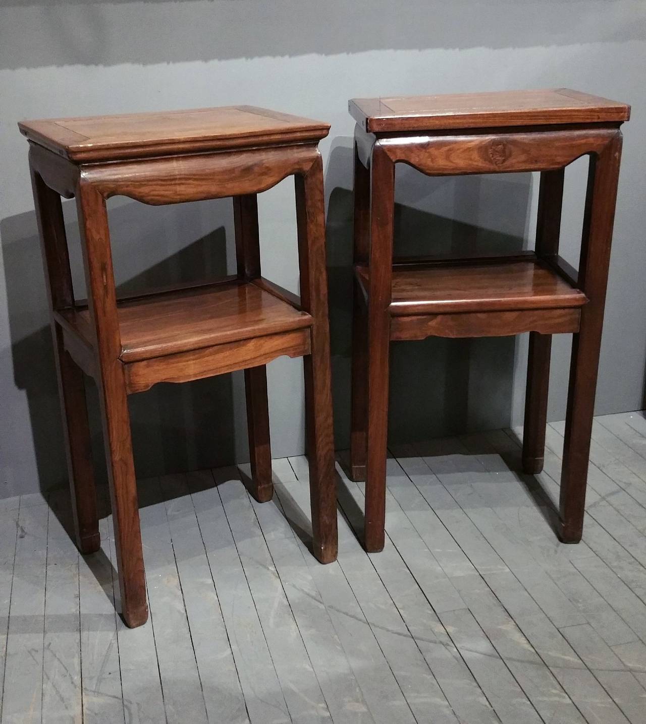 This simple but very appealing pair of Chinese hardwood side tables features a single central shelf with a shaped apron that also runs around the top. The table tops have a cross banded border and the wood overall has a rich, warm patina. Each table