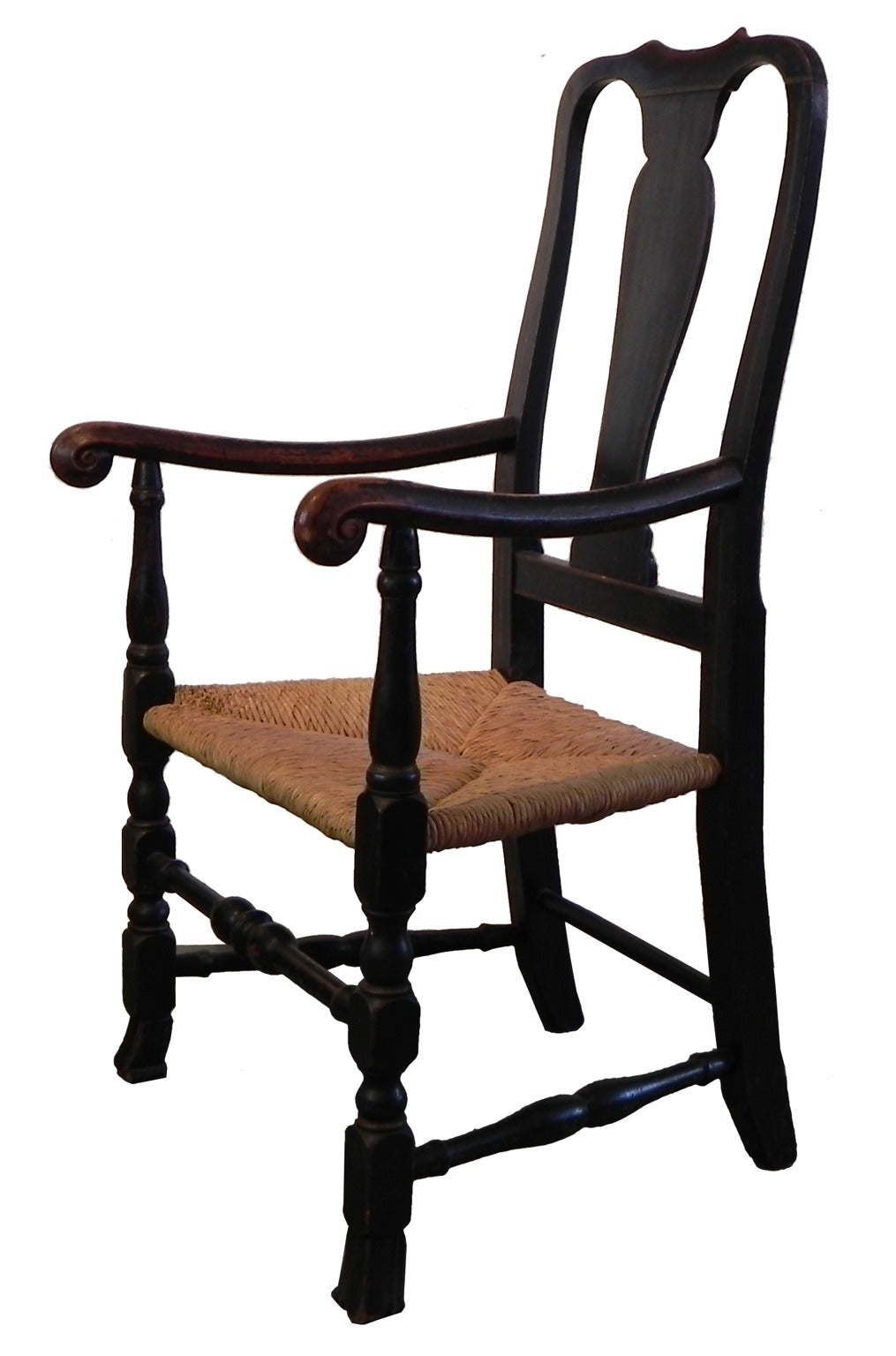 This is an armchair having elements of the early Queen Anne period with wonderfully proportioned curves to the top half of the chair. Ram’s horn hand holds highlight the outward scrolling arms, and enclose a rush seat with the original ash seat