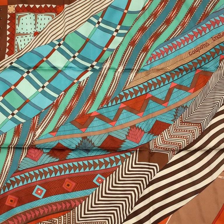 This authentic Hermes Coupons Indiens 90 cm Silk Scarf is pristine. Artist Ailine Honore and issued in 2008. Swirling patterned fabrics in shades of brown and turquoise. 100% silk. 
A237