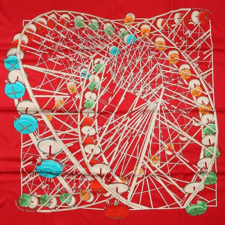 This authentic Hermes Grande Roue 90 cm Silk Scarf is new with the box.
 Designed by artist Dimitri Rybaltchenko and issued 2006. A bright red background features a ferris wheel with multi colored carriages and cheery riders. Made in France. 100%