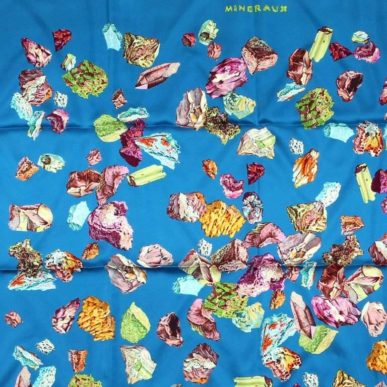 This authentic Hermes Mineraux 90 cm Silk Scarf is new and unworn. Designed by Hugo Grygkar originally in 1959. Blue background features a colorful array of various crystals and minerals in their natural state. Made in France. 100% silk. Proudly