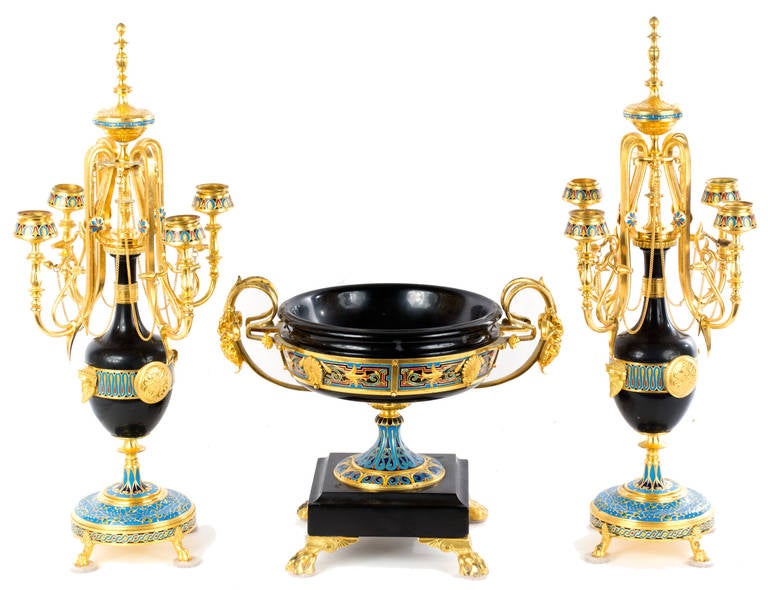 A three-piece French garniture with delicate arms, featuring finely chased, low-relief decoration and cloisonné enameling. A remarkable and harmonious combination of diverse styles (i.e. Chinese, French, and Egyptian) the garniture is a remarkable