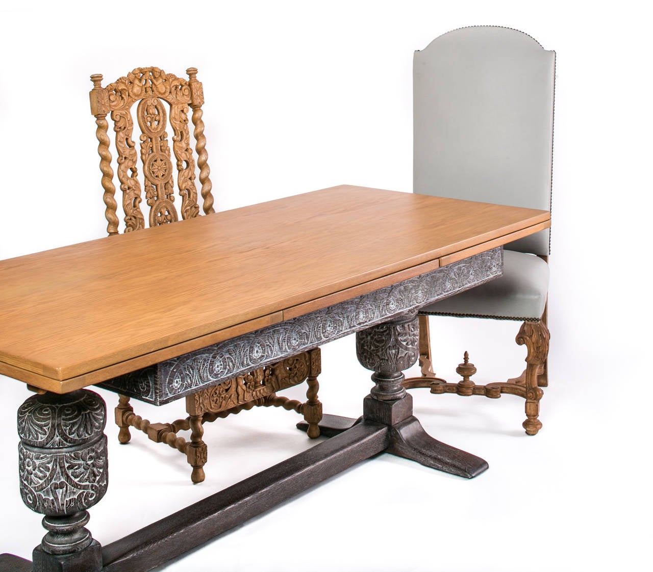 Refectory extendable english baroque dining table with hand carved chairs. Six chairs in black leather and two captain chairs in grey leather.