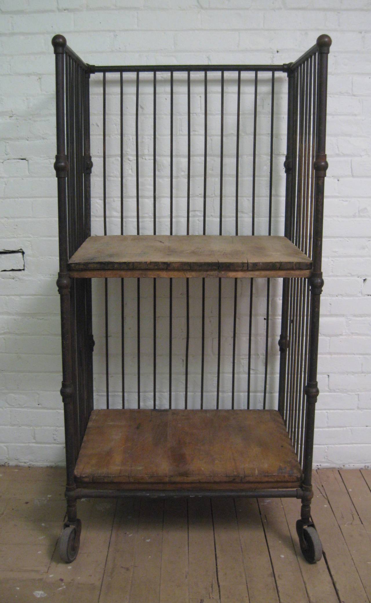 Fantastic deep rolling shelving unit, circa 1930-1940. Iron with two wood shelves on hard rubber wheels.