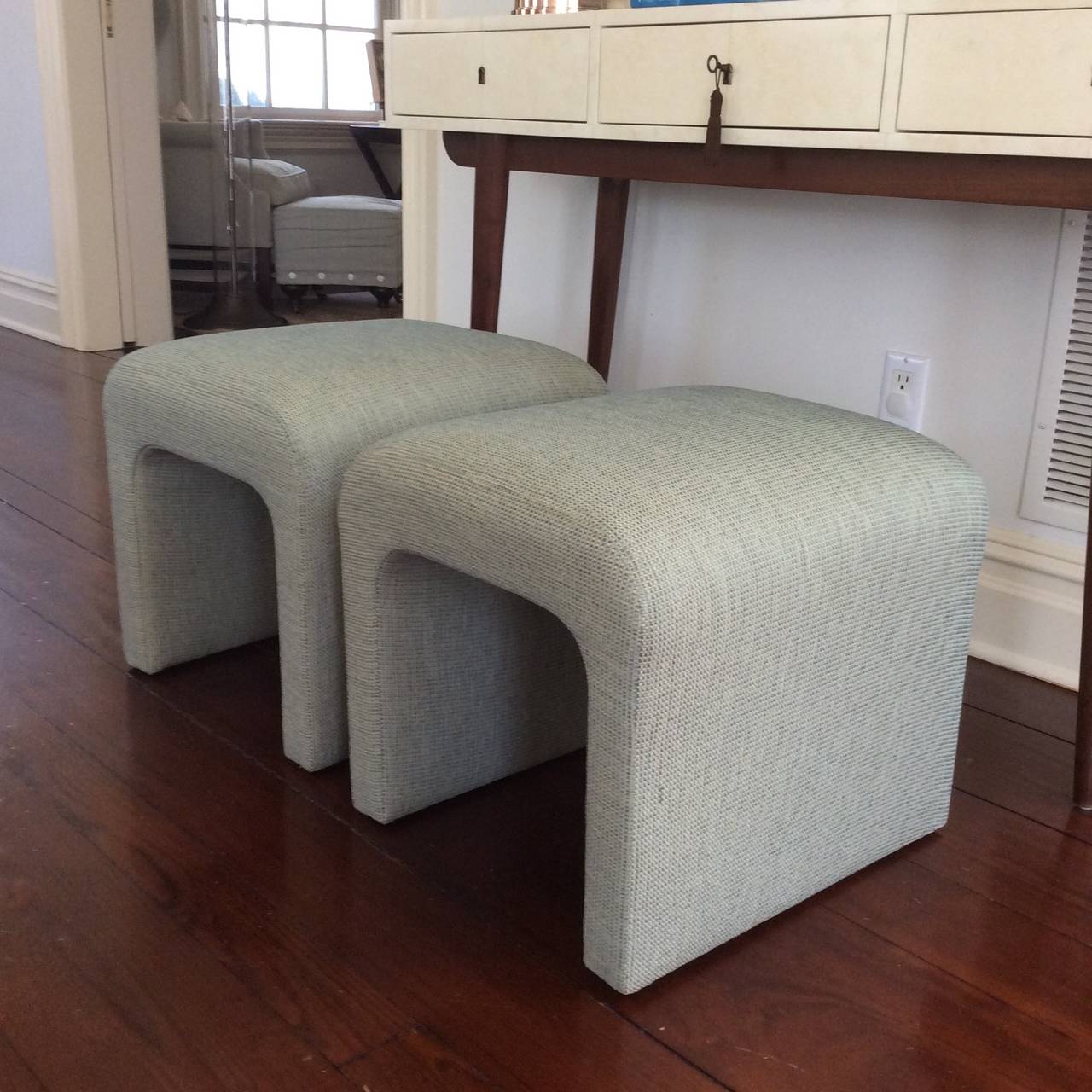 Pair of newly reupholstered waterfall ottomans circa 1970s. New foam on frame and  newly upholstered in Blue/green Kravet tweed fabric.  Versatile form to use a pull up seating or tuck away under a chic console table.