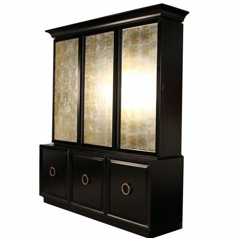 Rare, T.H. ROBSJOHN-GIBBINGS for WIDDICOMB, two-piece breakfront cabinet, with reverse silver-leafed glass panels (concealing interior shelves), over three door cabinet with large brass drop pulls. 
Cabinet was newly ebonized and in excellent