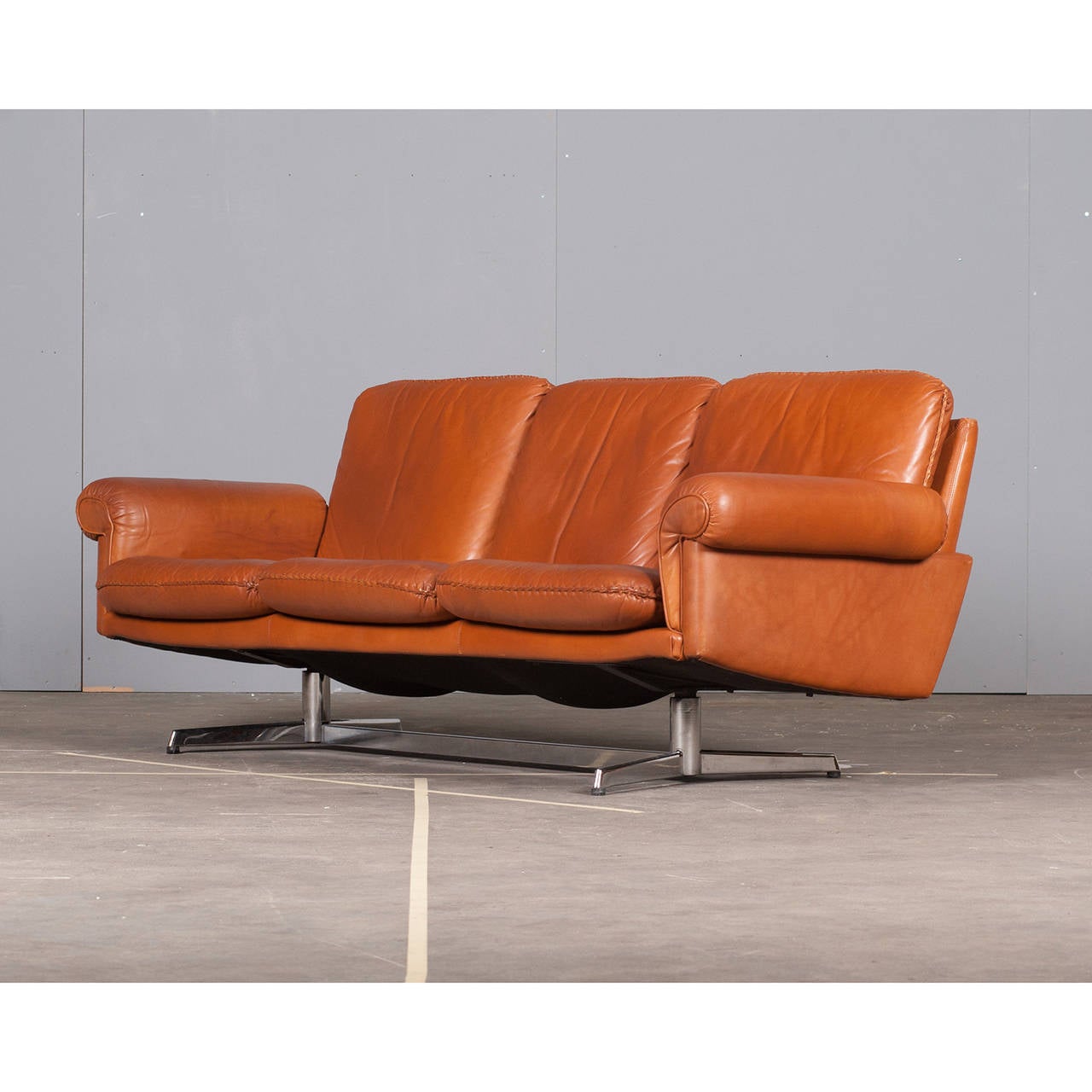 A beautiful and unique Danish caramel coloured leather sofa with rolled armrests and a cool steel base by De Sede, Switzerland. Very unique, this style of sofa is great for a room with a distinctive character, yet still has the comfort and