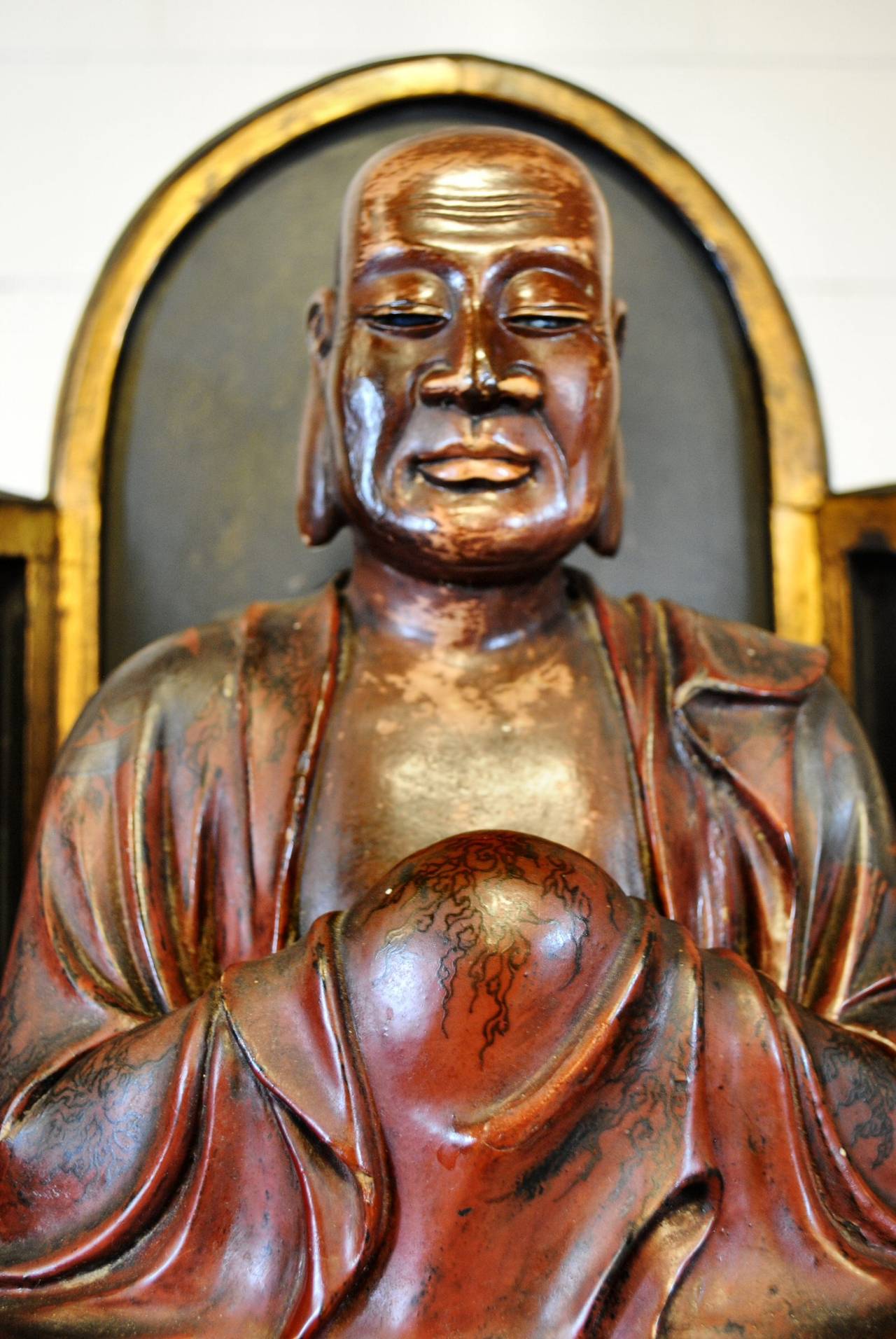 Carved antique Chinese seated Lohan Monk with original paint and gilt. The monk sits with a serene expression. His extended earlobes in reference to his capabilities of listening and understanding. His flowing robes are decorated with lotus flowers