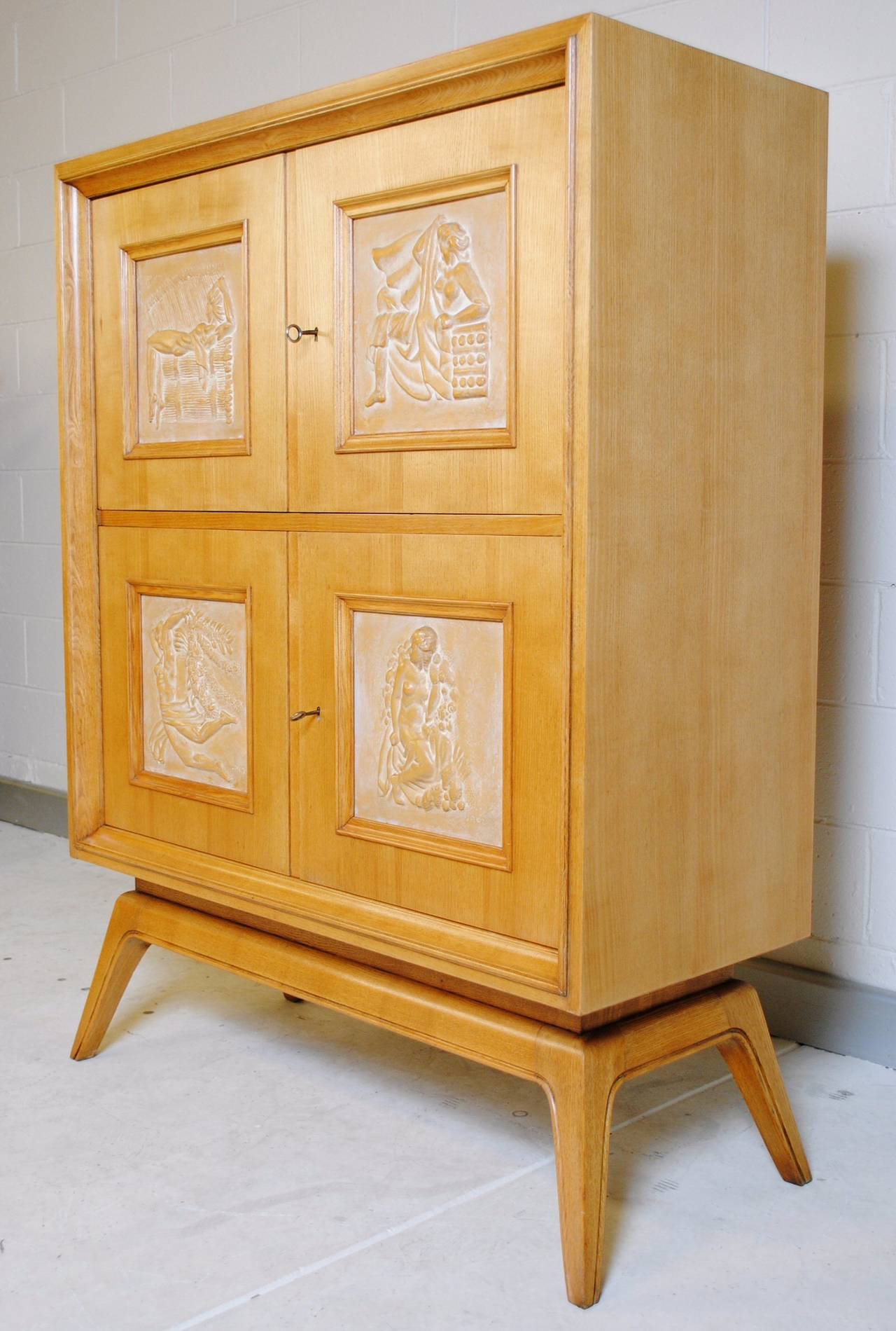 Early 1950s four door Oak cabinet inset with four relief terracotta panels. Each panel revealing a stylized woman and each one bearing a part signature reading 'JACZ'. The cabinet rests on four splayed legs, typical of the period.
