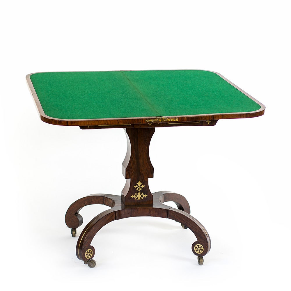 A 19th century English Regency rosewood veneered card table, with brass inlay. The piece is in excellent condition, with its original caster wheels and minimal damage to the veneer. The card table has a green felt top, which is not original to the