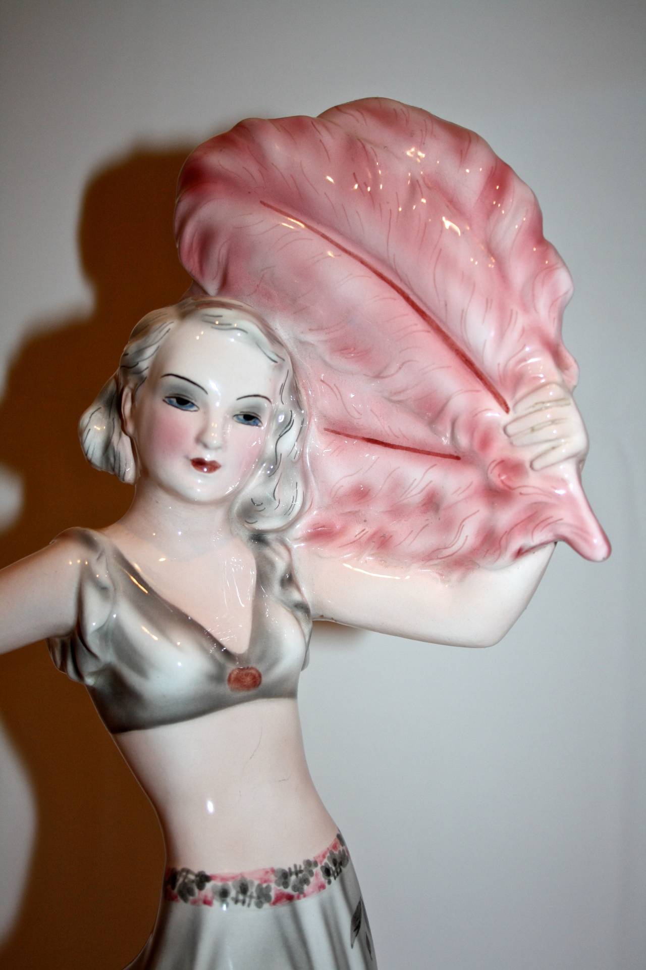 This Rare and Stunning Art Deco figure by Josef Lorenzl for Goldscheider featuring a young showgirl holding a large ostrich feather and holding out her beautiful skirt. The dress has colors of light grey, Charcoal and pink featuring a floral