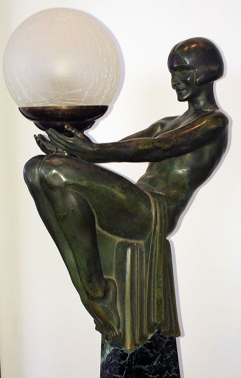 'Enigme' a Figural Lamp, circa 1925 of a partially nude woman balanced atop a marble obelisk with a glass globe in her outstretched arms.  Bronze on a marble obelisk with the original shop label still partially affixed to the marble.
Currently
