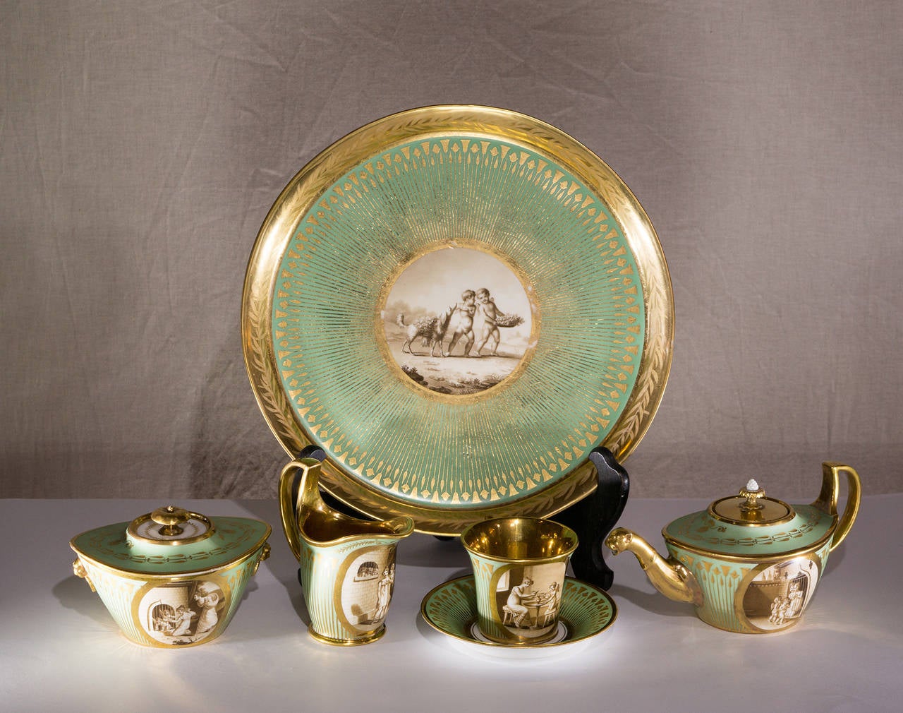 Pariser Porzellan-Solitär-Set von Dagoty und Honre:: bestehend aus: Teekanne mit Katzenkopfausguss:: Sucrier:: Milchkännchen:: Tasse und Untertasse und Tablett:: jeweils mit bemalten Tafeln von Amor bei verschiedenen Beschäftigungen:: der hellgrüne