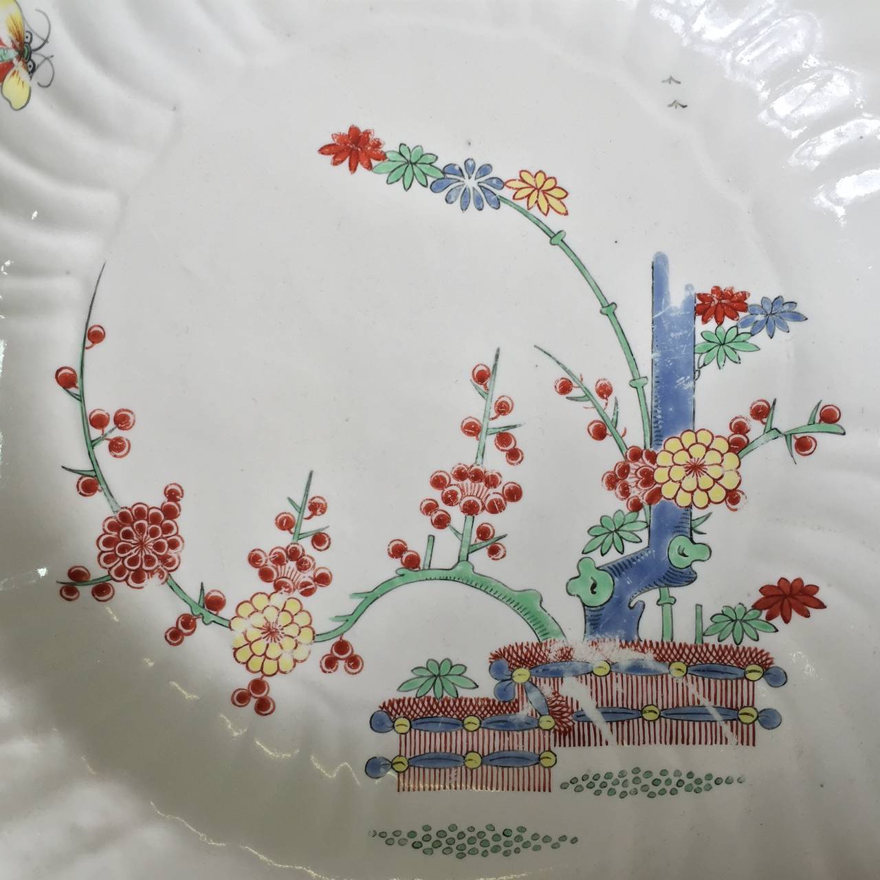Chantilly spiral fluted plate in the kakiemon manner, painted in bright enamels with a banded hedge pattern, a phoenix flying overhead, with various stylised flower heads and bugs on the rim and a brown line edge.           
Circa