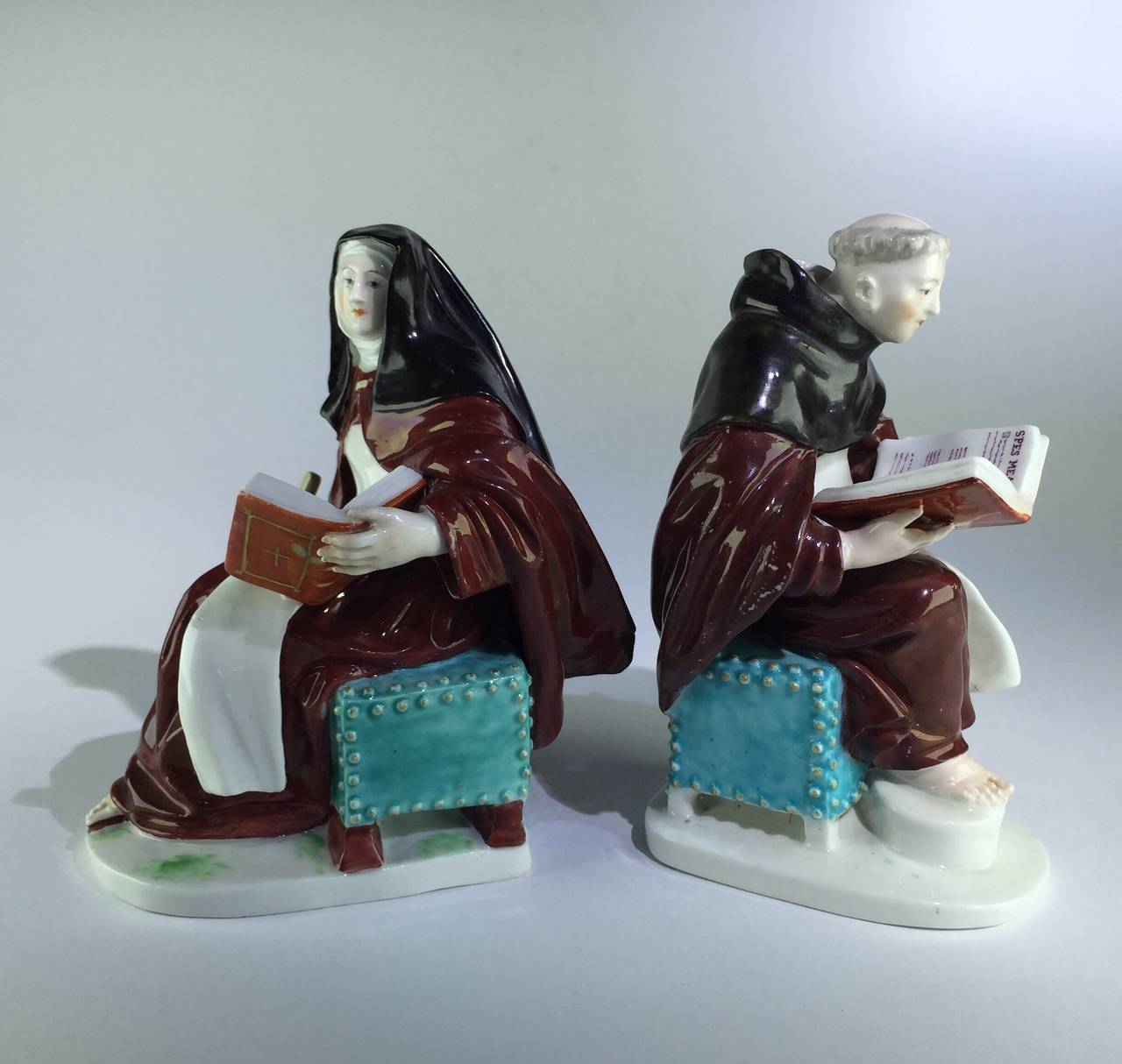 Rare pair of Derby religious figures, of a nun and a friar, each seated on a studded turquoise stool, dressed in brown habit and reading from a large red covered book,
circa 1760.

Ref. Bradshaw Derby figures p255. The pair are no. 105 on the