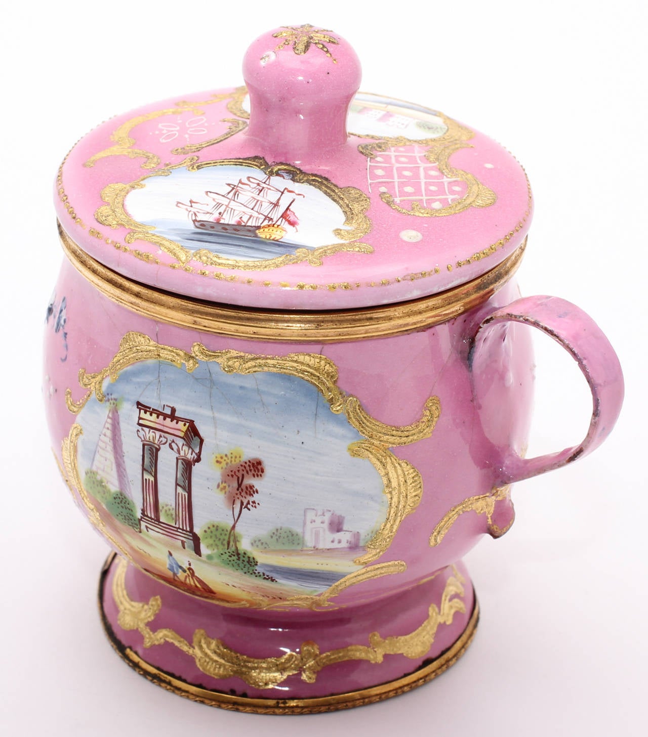 Rare English enamel covered cup or mustard pot, of typical form, decorated in bright pink ground with reserved panels of landscapes, including figures before a landscape and a fully rigged ship, with raised gold rococo frames and flourishes.     
