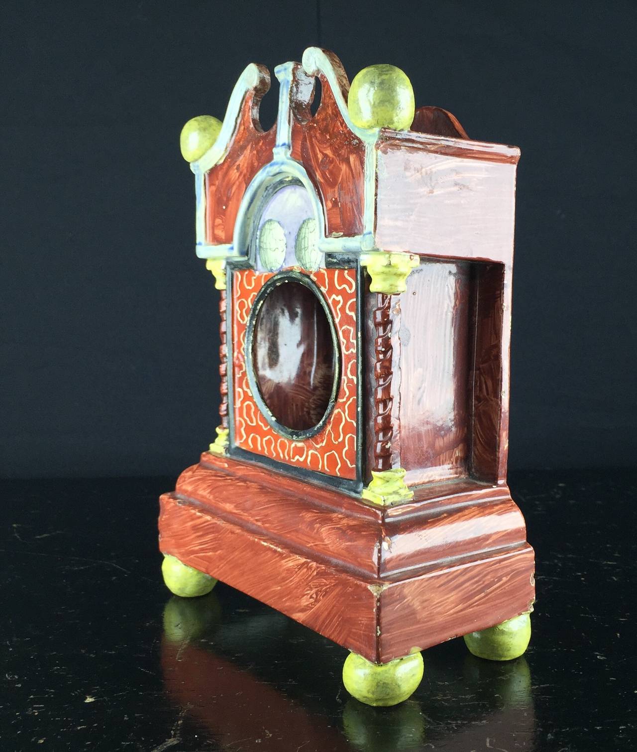 Staffordshire Pearlware model of a bracket clock, on a plinth base with ball feet, the face decorated with world globes, the broken pediment supported by moulded pillars, with open circular hole to display a pocket watch, a smaller hole and three