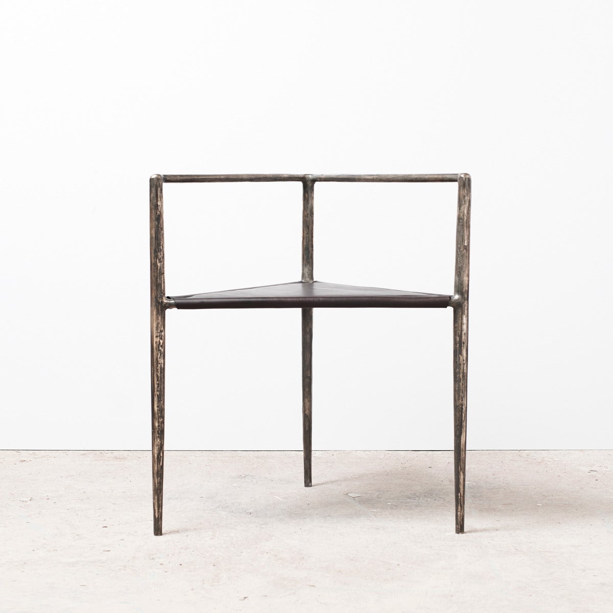 The Alchemy Chair by Rick Owens is conceptually established on a triangular prism wireframe. Its Brutalist bronze legs and arms are elegantly tapered and textured, comfortably dissected by a plane of black leather upholstery. Not only is the Alchemy