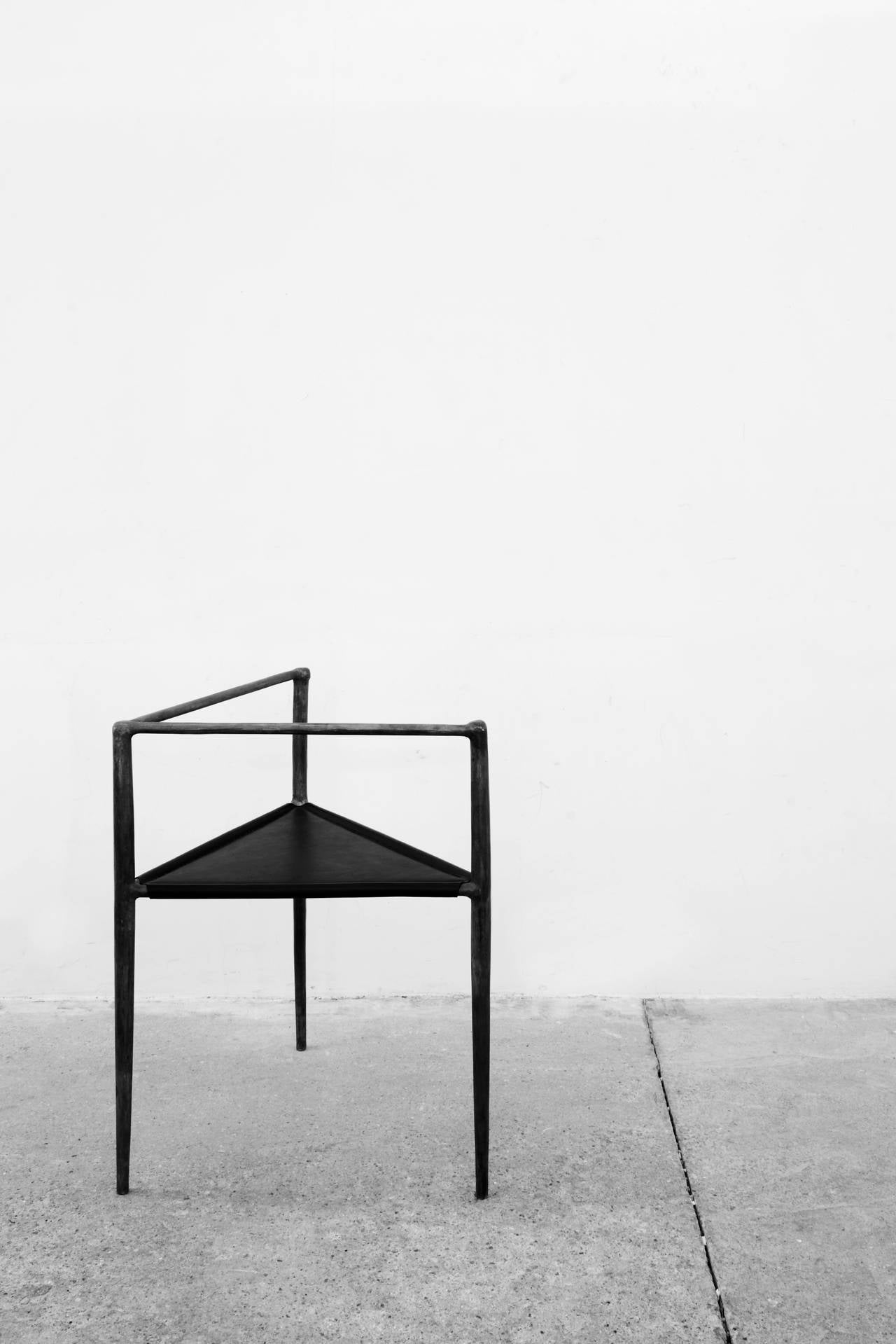 The alchemy chair by Rick Owens is conceptually established on a triangular prism wireframe. Its Brutalist bronze legs and arms are elegantly tapered and textured, comfortably dissected by a plane of black leather upholstery. Not only is the alchemy