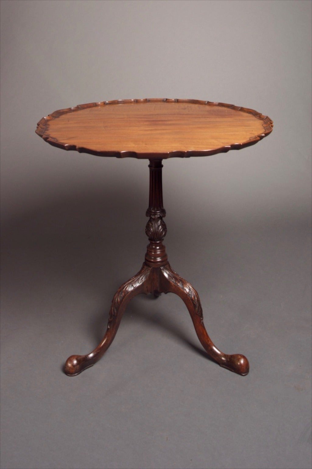 A George III tilt-top tea table, the top being of one single piece of Honduras mahogany. Having a piecrust & scalloped edge, the whole standing upon a fluted & turned column, tripod base with foliate carving to the knees. Original polish showing a