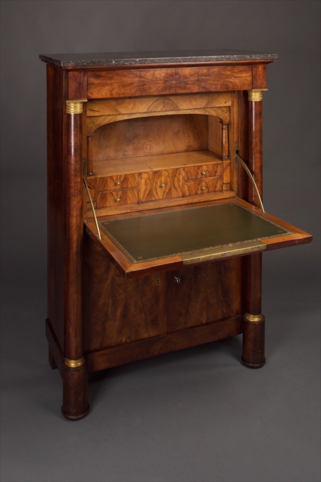 A 19th century secretaire abattant in the Empire taste. Bookmatched feathered mahogany, the interior of the desk being in pale bookmatched figured walnut. Gilt bronze mounts and grey marble top. Frieze drawer with the secretaire below, with a