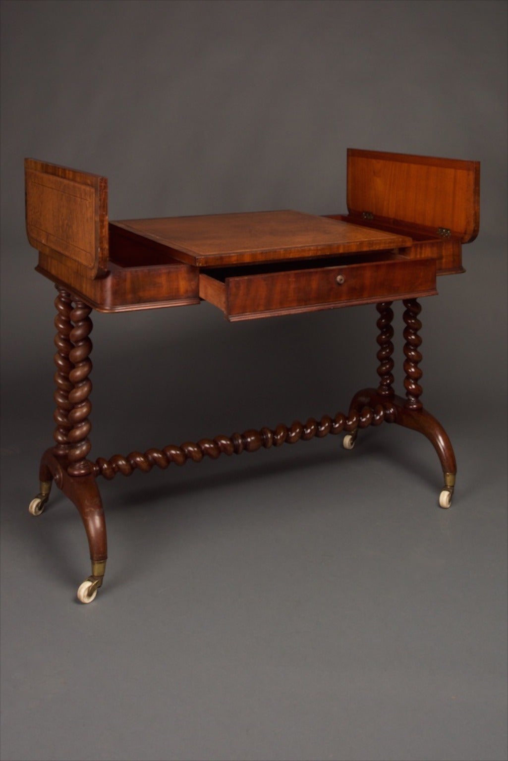 A William IV library table in mahogany. The table has one-drawer to the frieze and two fitted compartments to either side of the inset leather desktop. The whole standing upon turned barley-twist columns and curved tapered bases with their original
