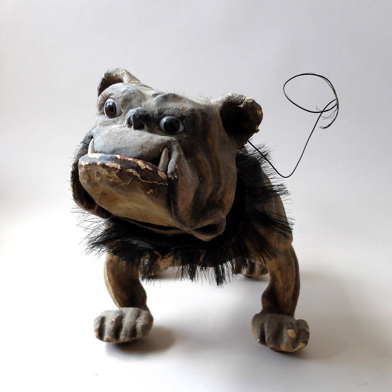 Flocked papier mâché toy bulldog, on wooden castors, with a nodding head, hair collar, glass eyes, and an articulated mouth that makes a growling noise when the lead is pulled.