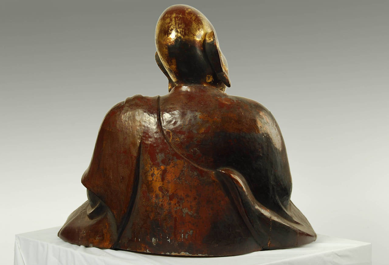 Antique Japanese carved statue of a Buddhist monk, Edo period, circa 18th century. Carved from wood with a brown lacquer and gold leaf finish.