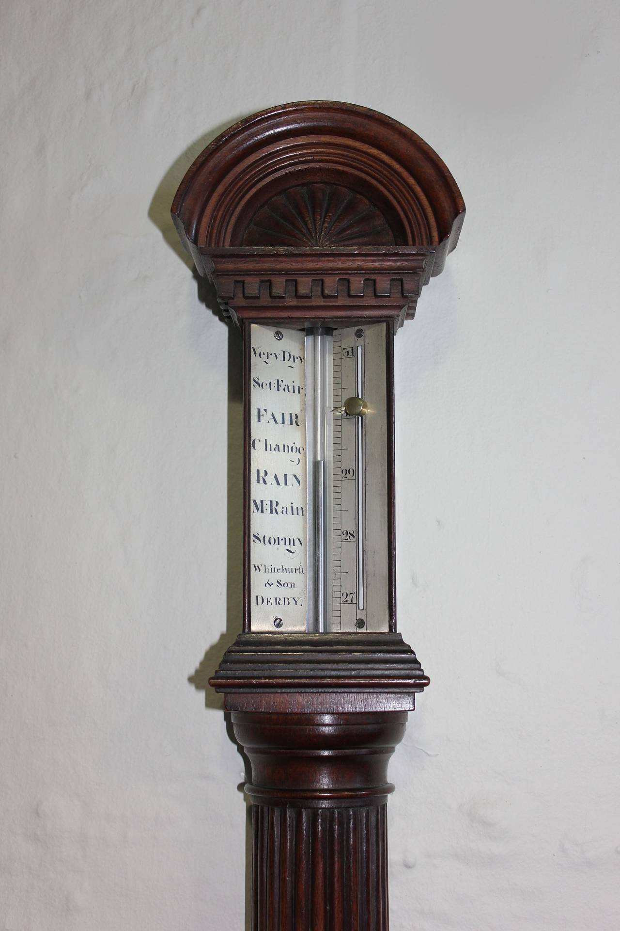 A Regency mahogany Barometer by Whitehurst & Son, Derby

Of cylindrical shape, the arched moulded pediment above an engraved metal scale and a turned reeded half-column, above a
stepped moulded rectangular pedestal, the scale inscribed