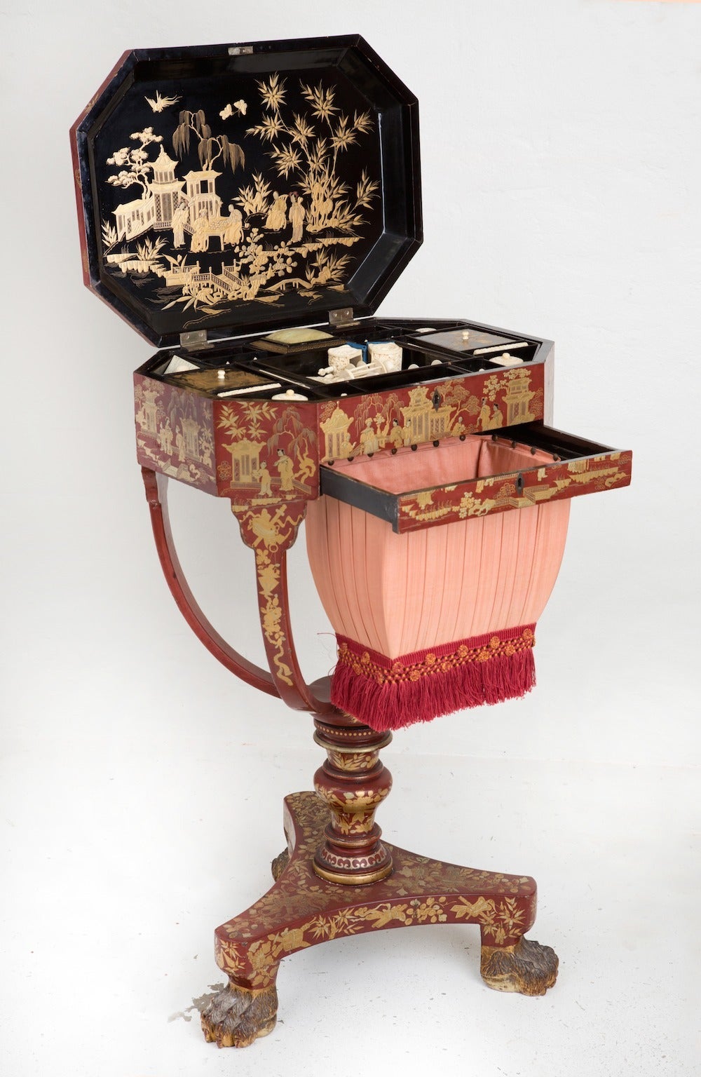 A very rare red lacquer Canton export ware Sewing Table
Raised on turned column on a tri-pod base with lion-paw feet below sliding pleated silk and fringe sewing basket box and hinged octagonal top with black and gilt scene opening to various