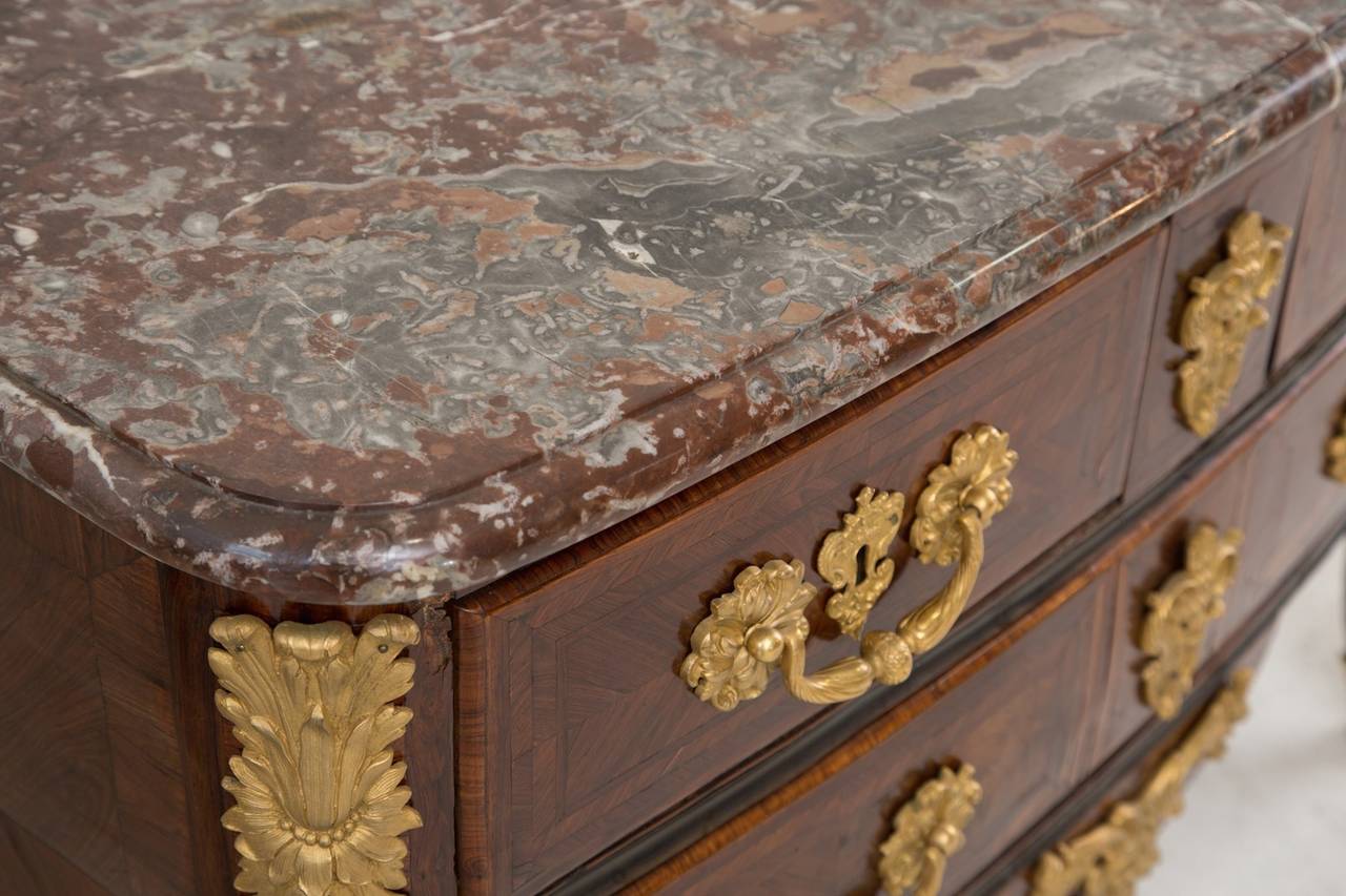 The rectangular white, grey and liver breccia marble moulded top above two short drawers and one long drawer, the shaped apron with applied ormolu foliate mount, with ornate foliate cast ormolu handles and key escutcheons, raised on cabriole legs