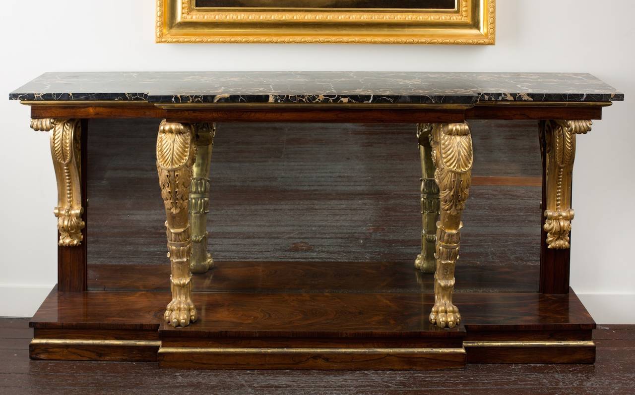 A very fine quality George IV period rosewood console table, in the Greek Revival taste, of break-front form, the underside mirrored, surmounted with veined black marble to plain frieze above two carved giltwood supports with lion paw feet, foliate