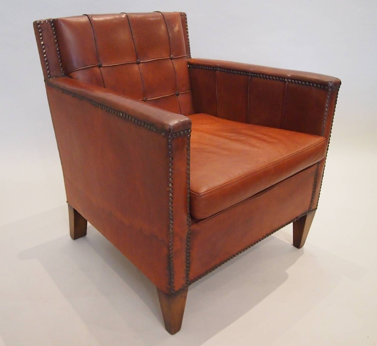 A pair of Art Deco leather library chairs with feather down seat cushions. All original brass studding intact.